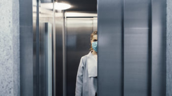 image of a woman wearing a protective face mask in an elevator with closing doors
