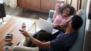 image of a couple on a couch, the man is watching TV and the woman is looking at her laptop